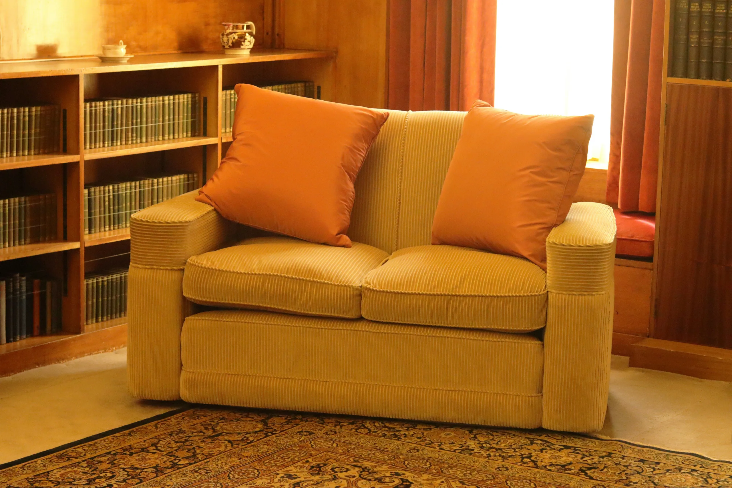 Reading Nook Lounge — Mood reference: a deep upholstered loveseat in a book-lined corner